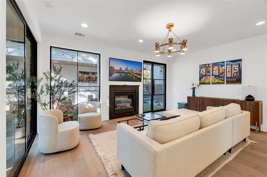 Living area featuring a glass covered fireplace, light wood-type flooring, a chandelier, and recessed lighting Living area featuring a glass covered fireplace, light wood-type flooring, a chandelier, and recessed lighting