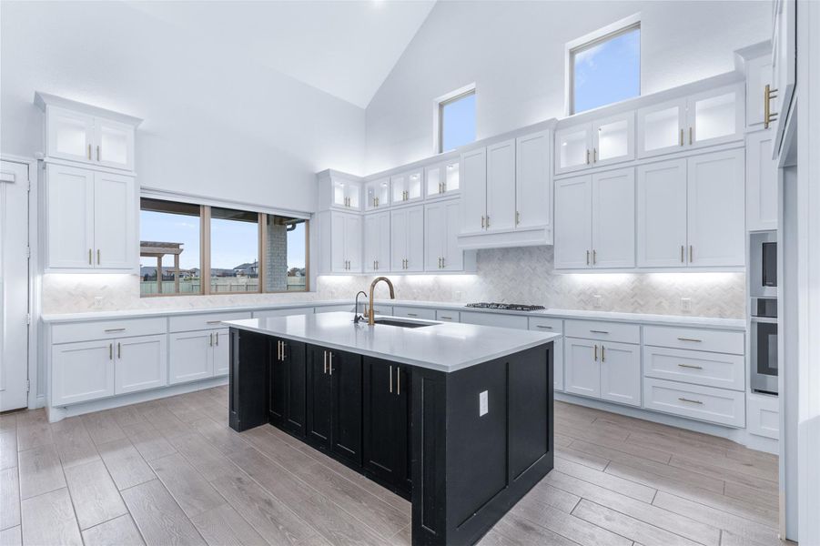 Kitchen featuring glass insert cabinets, dark cabinetry, white cabinetry, high vaulted ceiling, and a kitchen island with sink