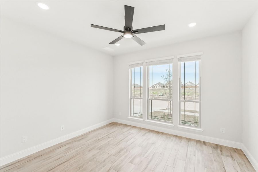 Empty room with light wood floors, ceiling fan, and three large windows with neighborhood view Empty room with light wood floors, ceiling fan, and three large windows with neighborhood view