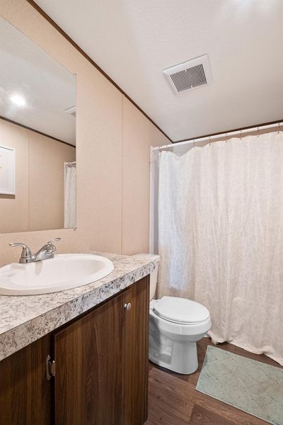 Full bath with crown molding, vanity, curtained shower, dark wood finished floors, and a textured ceiling