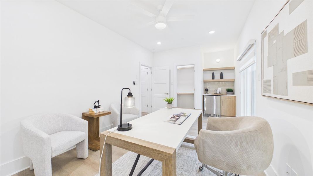 Bright and modern home office with minimalist decor, featuring a sleek desk, comfortable chairs, and ample natural light. The room includes built-in shelving and a small kitchenette area for convenience.
