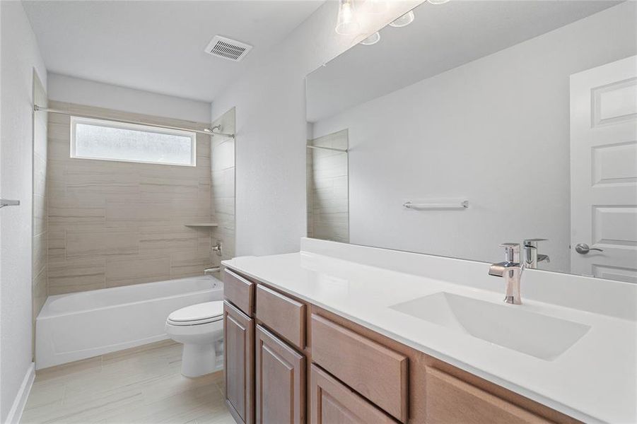 Secondary bath features tile flooring, bath/shower combo with tile surround, white stained wood cabinets, beautiful light countertops, mirror, dark, sleek fixtures and modern finishes.