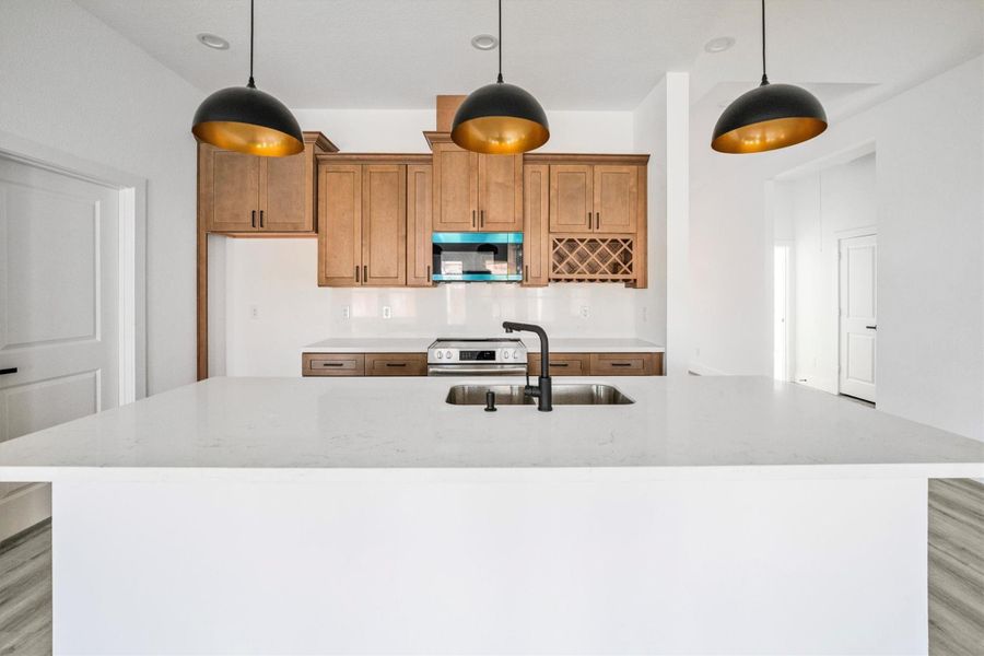 Modern kitchen with a large white island, black sink fixtures, and pendant lighting. Features wooden cabinetry, stainless steel appliances, and a built-in wine rack. Bright and open layout.