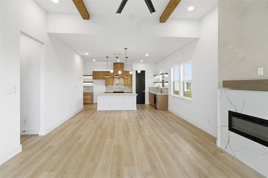 Unfurnished living room featuring beam ceiling, light wood-type flooring, a high end fireplace, a ceiling fan, and recessed lighting
