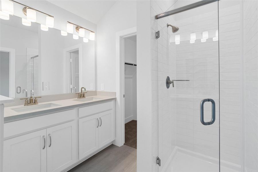A bright and functional primary bath offering dual sinks for busy mornings, a large mirror, soaking tub, and a modern glass-enclosed shower, creating a serene and efficient space.