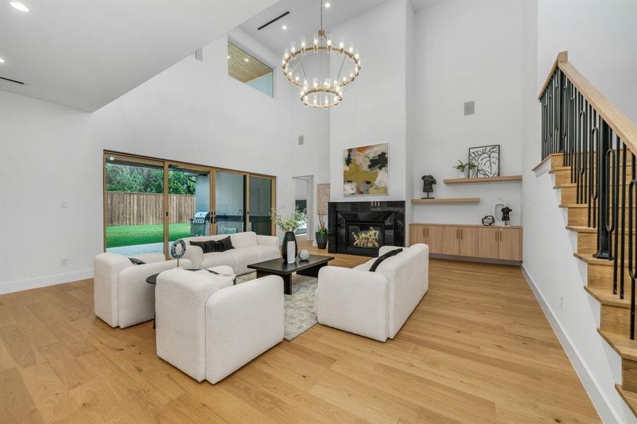 Living area with stairway, a glass covered fireplace, light wood-style flooring, a chandelier, and a towering ceiling