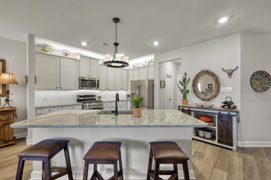 Designer kitchen featuring an oversized granite island with breakfast bar seating, abundant cabinetry, stainless steel appliances, gas range, subway tile backsplash, and seamless flow to the main living and dining areas. Designer kitchen featuring an oversized granite island with breakfast bar seating, abundant cabinetry, stainless steel appliances, gas range, subway tile backsplash, and seamless flow to the main living and dining areas.