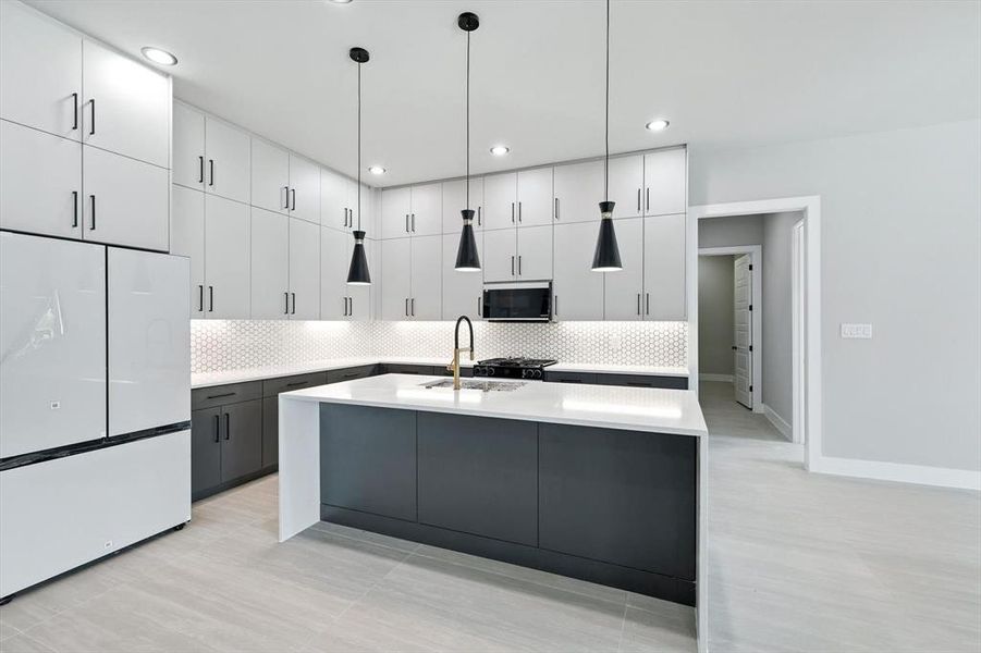 Kitchen featuring white cabinets, freestanding refrigerator, a center island with sink, backsplash, and hanging light fixtures Kitchen featuring white cabinets, freestanding refrigerator, a center island with sink, backsplash, and hanging light fixtures