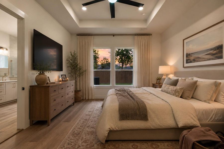The well-designed primary bedroom features an 11-foot tray ceiling with a ceiling fan and recessed lighting. (Virtually staged at sunset) The well-designed primary bedroom features an 11-foot tray ceiling with a ceiling fan and recessed lighting. (Virtually staged at sunset)