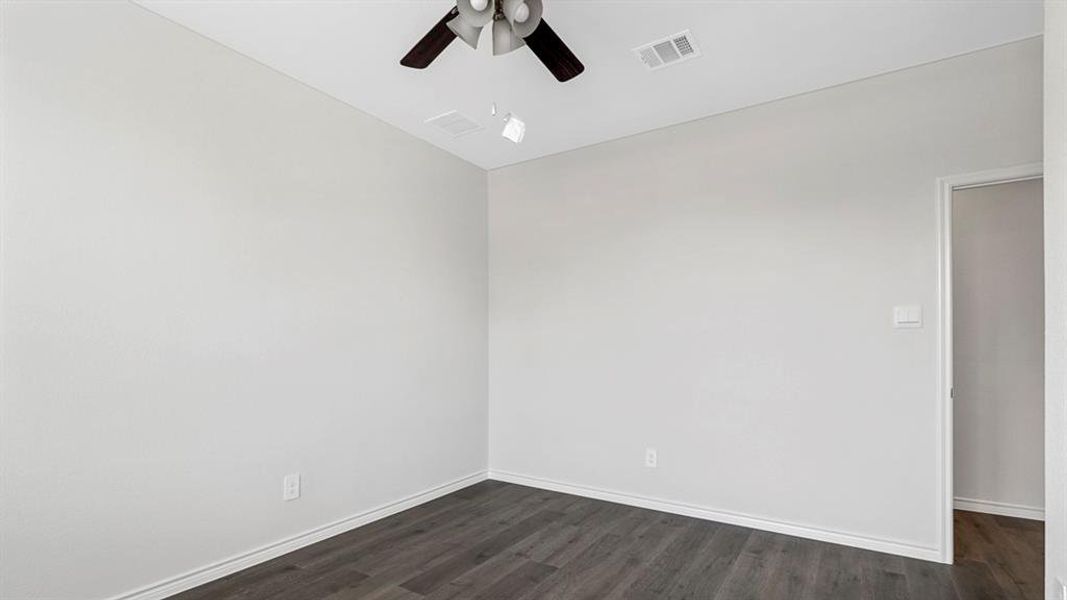 Room featuring light neutral walls, wood-finish flooring, white baseboards, and a ceiling fan with dark blades