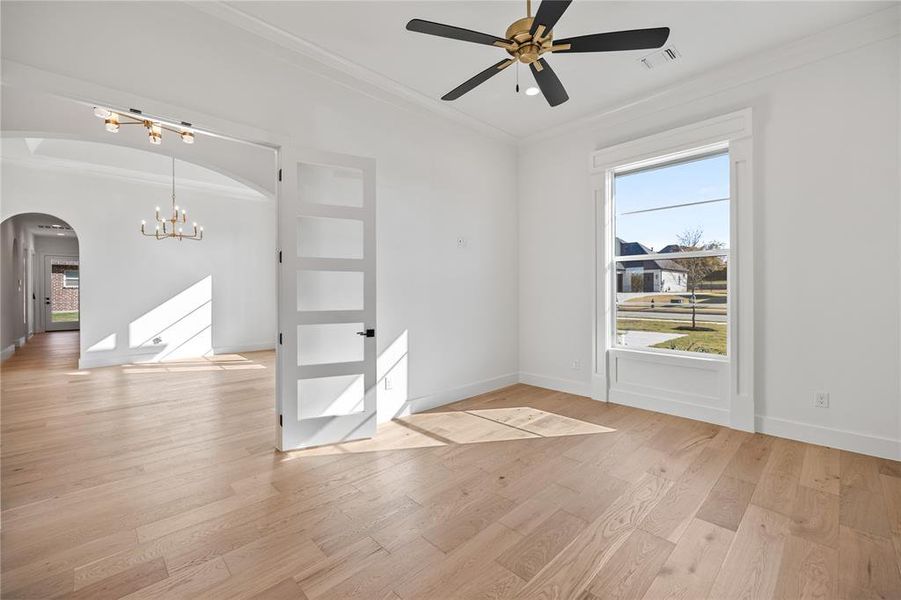 Spare room with ornamental molding, light wood-style floors, a chandelier, ceiling fan, and arched walkways Spare room with ornamental molding, light wood-style floors, a chandelier, ceiling fan, and arched walkways