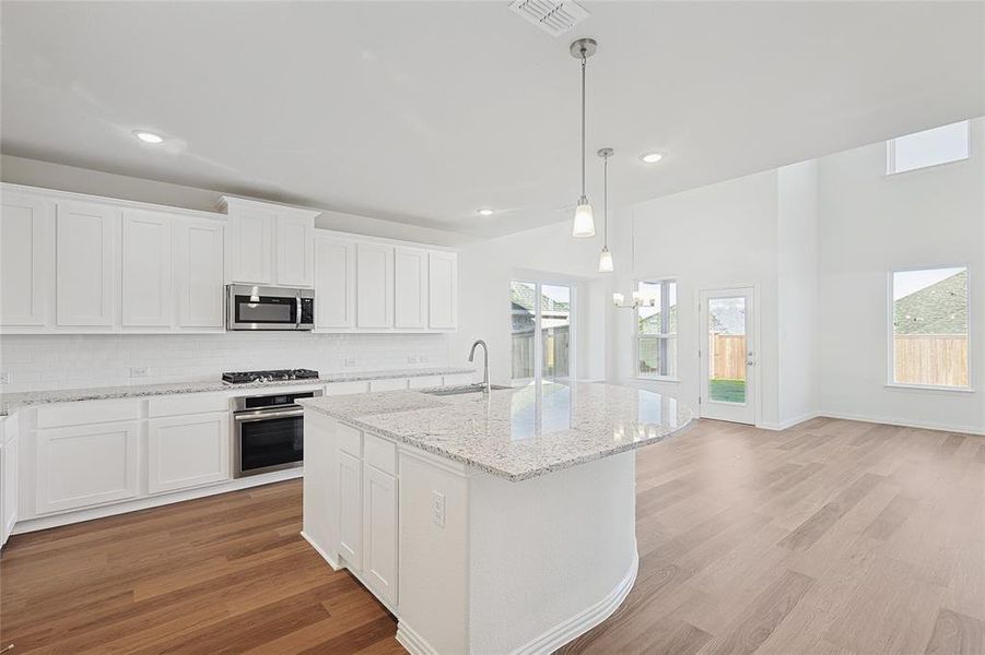 Kitchen with a wealth of natural light, white cabinetry, stainless steel appliances, and a kitchen island with sink