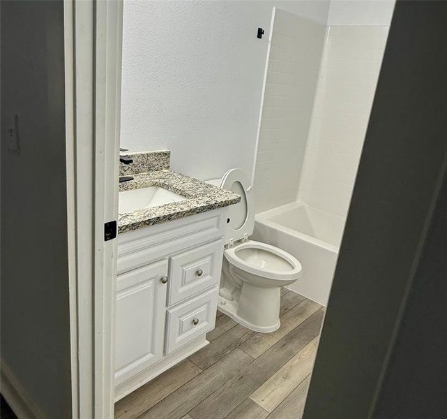 Full bath featuring vanity, light wood-type flooring, shower / bathtub combination, and a textured wall
