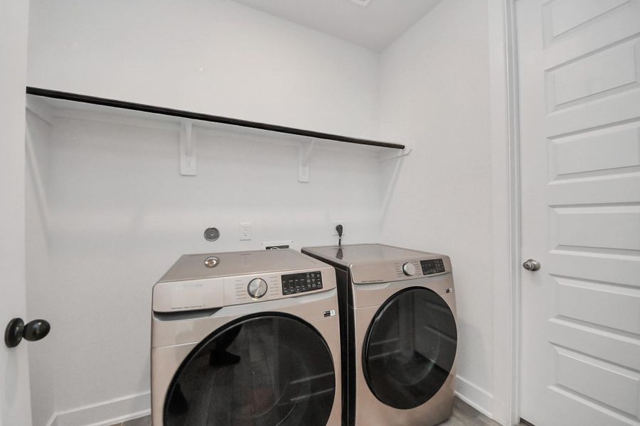This photo shows a modern laundry room with a sleek washer and dryer set. The space is bright with white walls, a shelf for storage, and a white paneled door. This photo shows a modern laundry room with a sleek washer and dryer set. The space is bright with white walls, a shelf for storage, and a white paneled door.