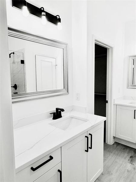 Full bathroom with two vanities, a shower stall, and light wood finished floors