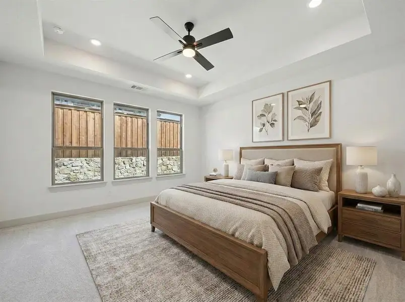 Spacious bedroom featuring a tray ceiling with recessed lighting, three large windows, a ceiling fan, and light-toned carpeting