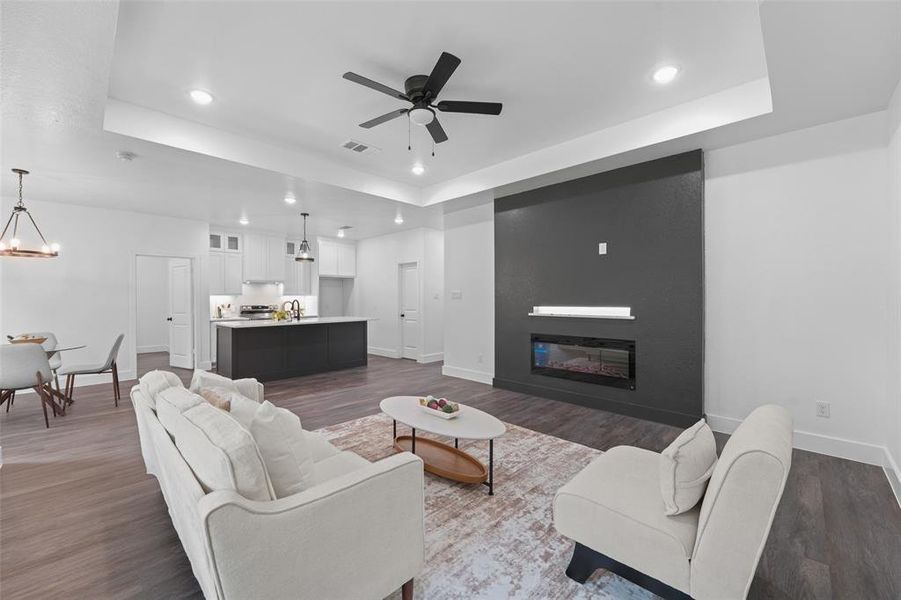 Open-concept living space featuring wood-finish flooring, a contemporary dark accent wall with an integrated electric fireplace, and recessed lighting Open-concept living space featuring wood-finish flooring, a contemporary dark accent wall with an integrated electric fireplace, and recessed lighting