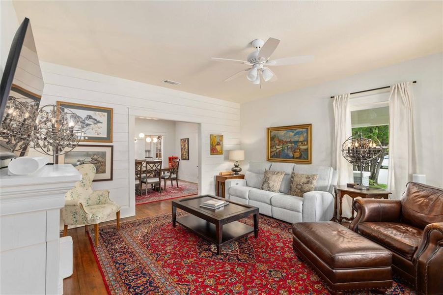 Living area with wood-finish flooring, white shiplap accent wall, white ceiling fan, and a wide entryway to a dining space