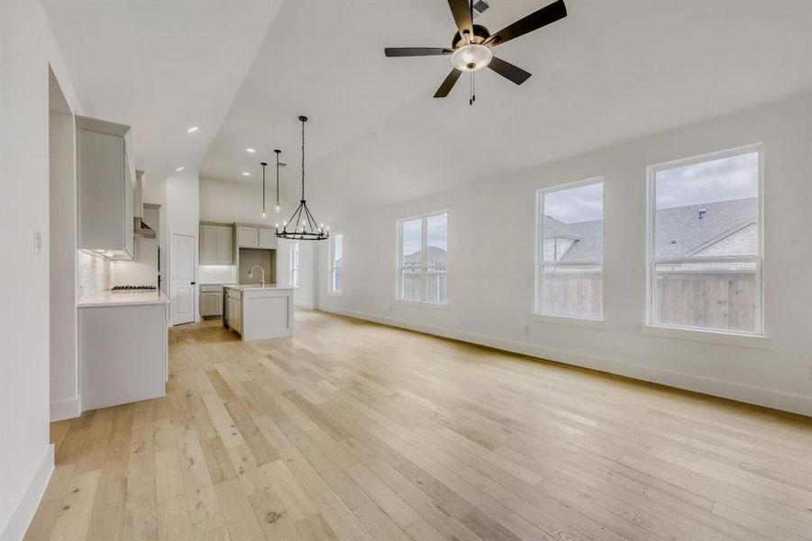 Unfurnished living room featuring suspended lighting, light wood-style flooring, ceiling fan, and lofted ceiling Unfurnished living room featuring suspended lighting, light wood-style flooring, ceiling fan, and lofted ceiling