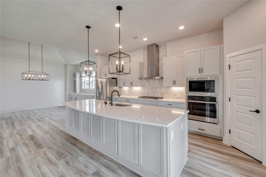 Kitchen featuring a central island with white countertop, light gray cabinetry, stainless steel appliances, decorative backsplash, and wood-finish flooring