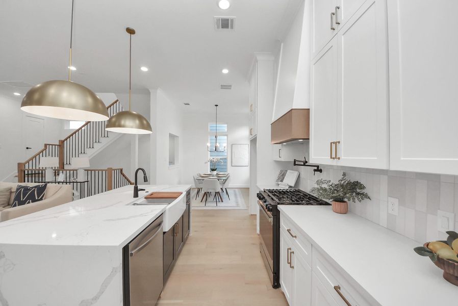 Experience this modern, open-concept kitchen with sleek white cabinetry, a large marble island, and elegant pendant lighting. The kitchen flows seamlessly into the dining area, with a view of the staircase leading to the upper floor, enhancing the spacious feel.