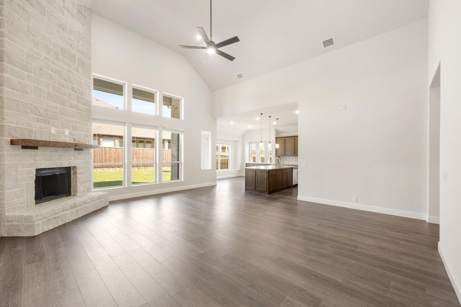 Open living room with vaulted ceiling, stone fireplace, hardwood floors, and open kitchen beyond Open living room with vaulted ceiling, stone fireplace, hardwood floors, and open kitchen beyond