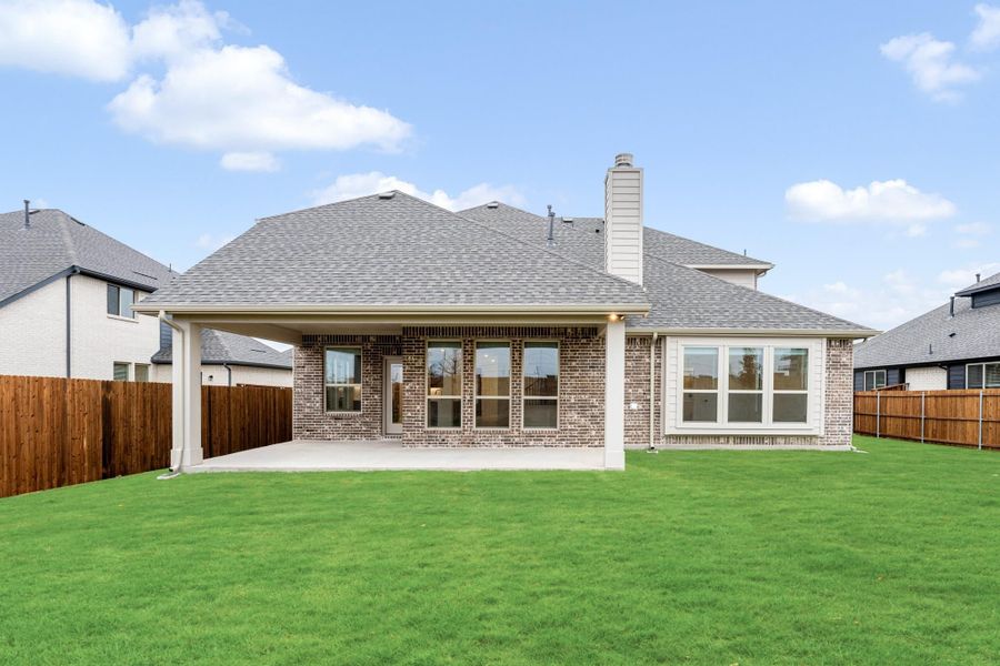 Brick home rear exterior with covered patio, chimney, and fenced backyard with green lawn Brick home rear exterior with covered patio, chimney, and fenced backyard with green lawn
