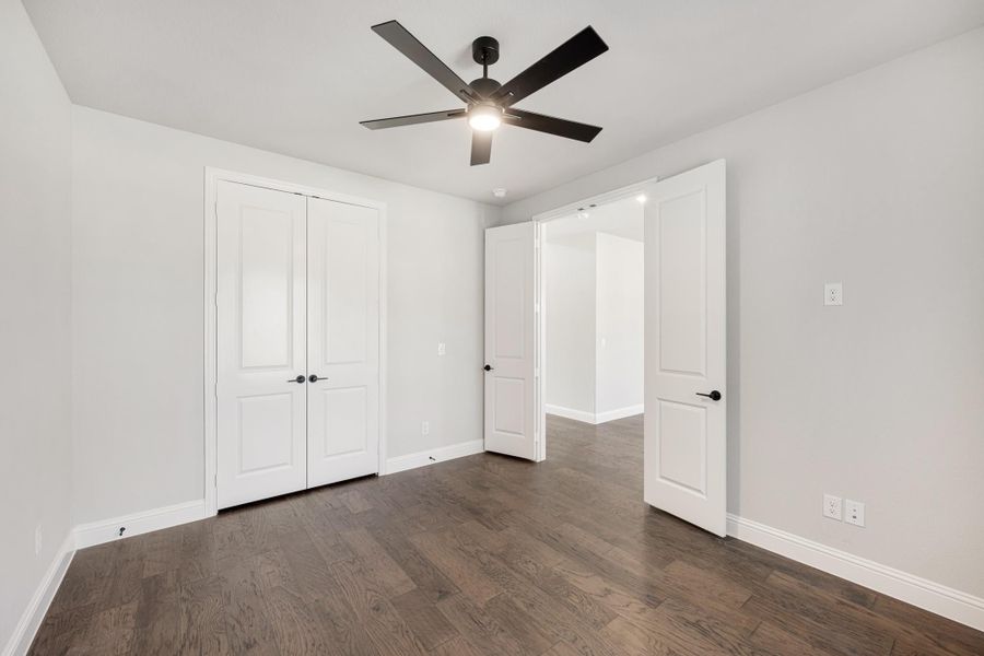 Empty bedroom with dark hardwood floors, ceiling fan, and double closet doors with black hardware Empty bedroom with dark hardwood floors, ceiling fan, and double closet doors with black hardware