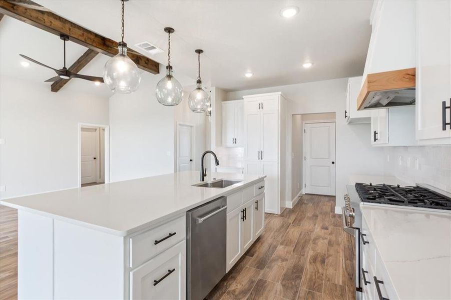 Kitchen featuring custom range hood, light countertops, appliances with stainless steel finishes, a sink, and wood finished floors