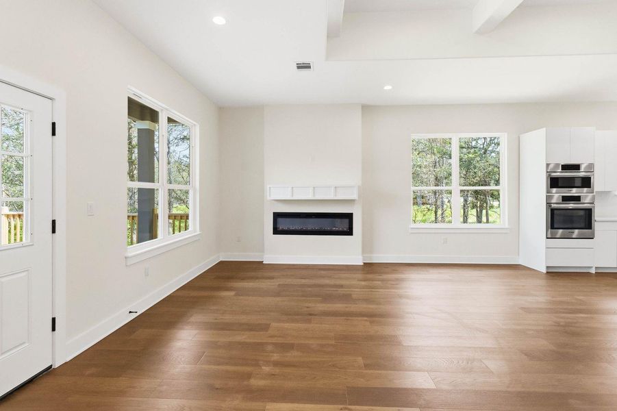 Hardwood floors stretch across this open-concept space, featuring a modern fireplace and bright windows. Hardwood floors stretch across this open-concept space, featuring a modern fireplace and bright windows.