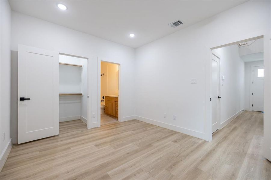 Alternate view of the first-floor bedroom: This spacious room features wood-look LVP flooring, recessed lighting, and a large window that fills the space with natural light. It also offers a view of the generously sized walk-in closet for added convenience