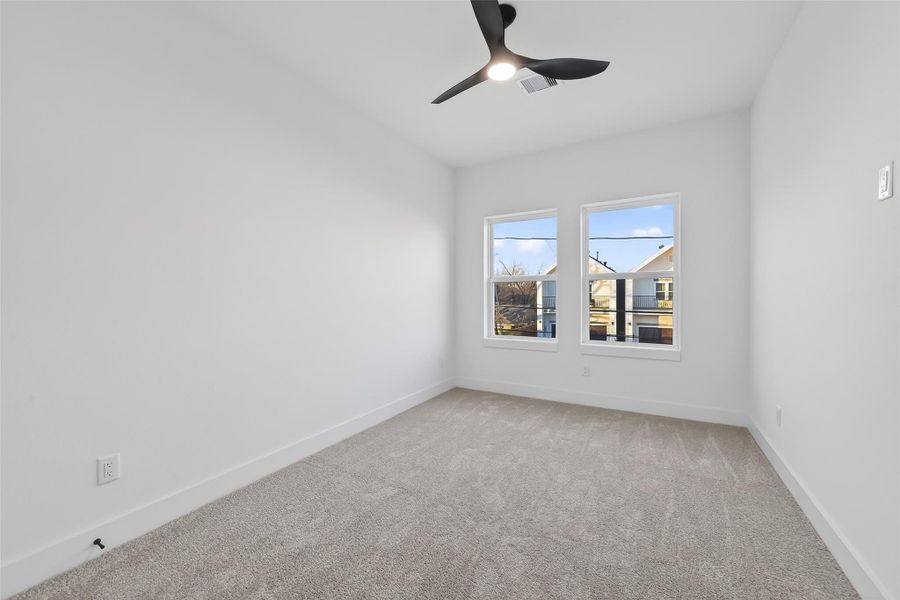 This room is bright and airy, featuring neutral carpeting and walls. It has two large windows for natural light and a modern ceiling fan. Perfect for a bedroom or office space.