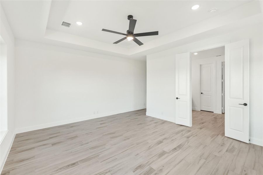 Empty bedroom with tray ceiling, ceiling fan, light wood floors, and two white doors Empty bedroom with tray ceiling, ceiling fan, light wood floors, and two white doors