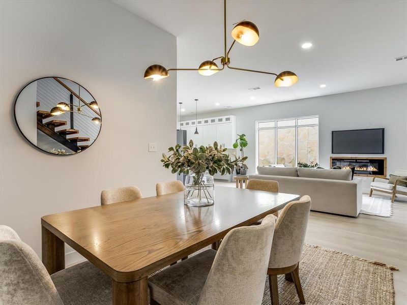 Open-concept dining area with a linear chandelier, wood-finish flooring, and a built-in fireplace Open-concept dining area with a linear chandelier, wood-finish flooring, and a built-in fireplace