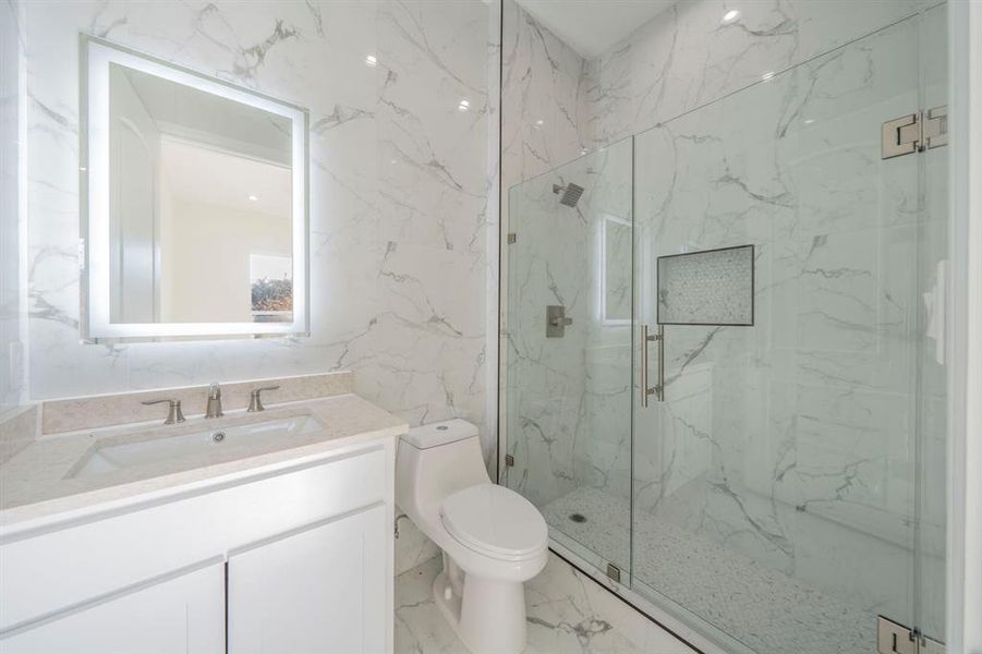 Bathroom featuring stone wall, vanity, a marble finish shower, and marble tiled flooring Bathroom featuring stone wall, vanity, a marble finish shower, and marble tiled flooring