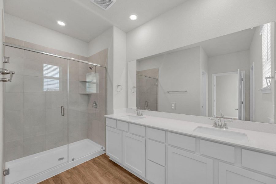Full bathroom with double vanity, a shower stall, and light wood-style floors
