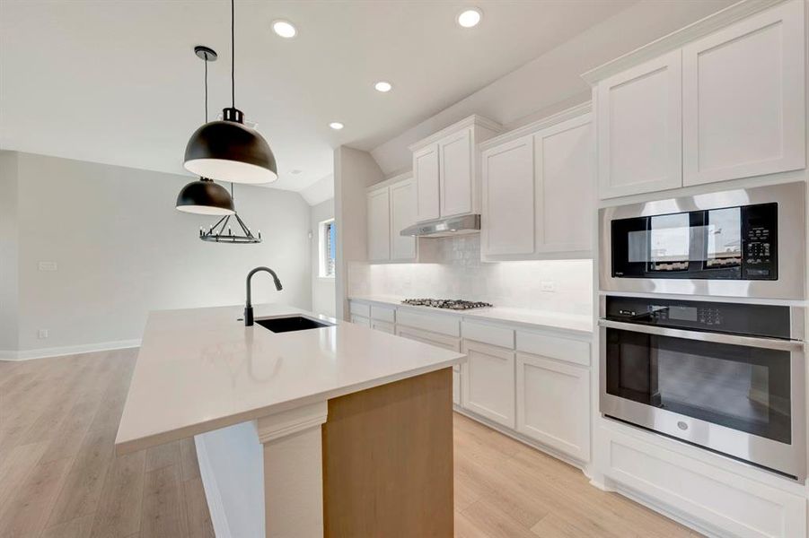 Kitchen with white cabinetry, stainless steel appliances, an island with sink, light wood finished floors, and vaulted ceiling