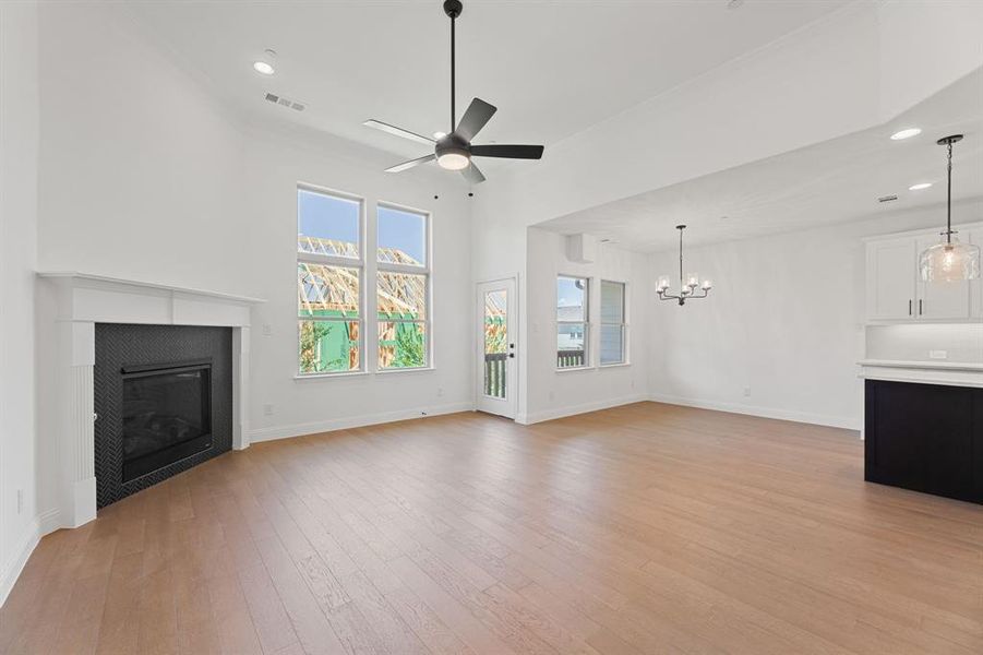 Unfurnished living room with recessed lighting, light wood finished floors, a fireplace, ceiling fan, and a chandelier Unfurnished living room with recessed lighting, light wood finished floors, a fireplace, ceiling fan, and a chandelier