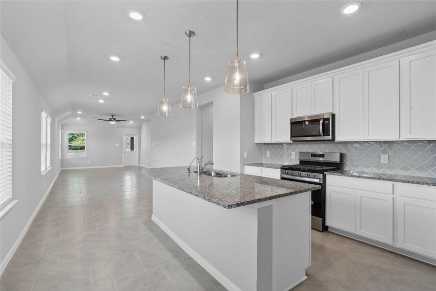 As you step past the entryway, you are immediately welcomed by a bright, open-concept kitchen that serves as the home's focal point. The space feels clean and modern, anchored by a large granite-topped island that seamlessly connects the cooking area to a long, light-filled living space.