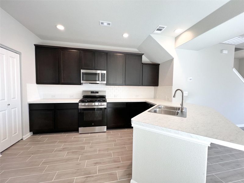 Kitchen featuring visible vents, a peninsula, stainless steel appliances, a sink, and backsplash Kitchen featuring visible vents, a peninsula, stainless steel appliances, a sink, and backsplash