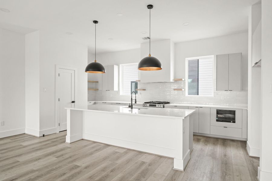 This gourmet island kitchen with decorative pendant lights, offers sleek cabinets with soft-close doors and drawers highlighted by quartz counter with a subway tile back splash and under-cabinet lighting. A spacious pantry is located on the left. This gourmet island kitchen with decorative pendant lights, offers sleek cabinets with soft-close doors and drawers highlighted by quartz counter with a subway tile back splash and under-cabinet lighting. A spacious pantry is located on the left.