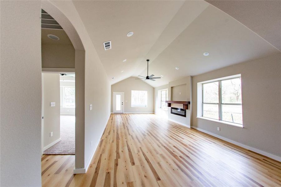 Unfurnished living room with lofted ceiling, arched walkways, light wood-style flooring, a glass covered fireplace, and plenty of natural light