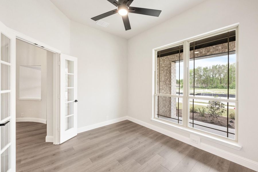 Empty room with hardwood floors, ceiling fan, large window, and French doors leading to adjacent space