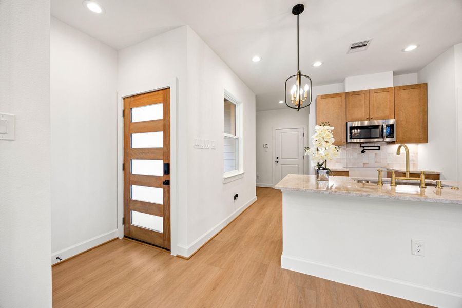 Welcoming entryway with a striking modern wood front door featuring frosted glass panels, allowing natural light to flow inside. Warm wood floors, recessed lighting, and crisp white walls create a bright, open, and contemporary atmosphere that sets the tone for the home.