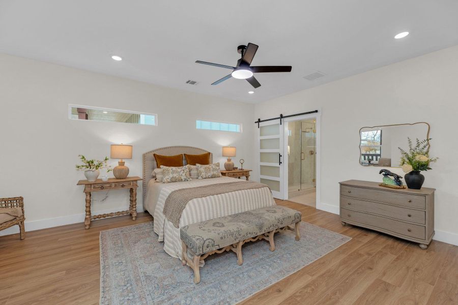 Bedroom featuring a barn door,  a ceiling fan, connected bathroom, and recessed lighting. Seating area.