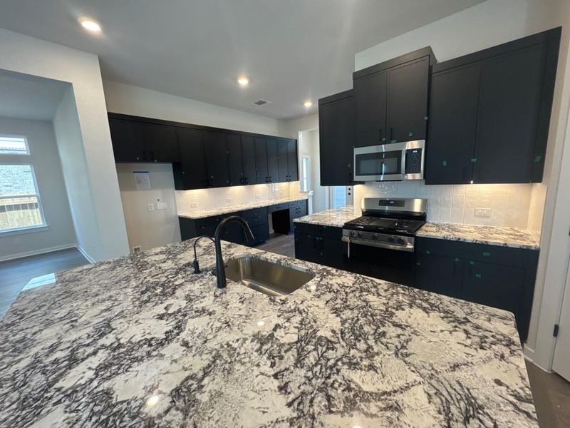 Kitchen featuring dark cabinetry, tasteful backsplash, light stone counters, stainless steel appliances, and recessed lighting Kitchen featuring dark cabinetry, tasteful backsplash, light stone counters, stainless steel appliances, and recessed lighting