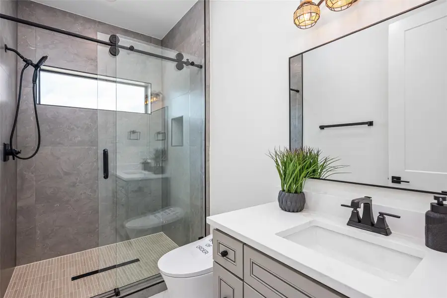 This en suite bath features a walk-in shower with sliding glass doors, accent mirrors, elevated lighting, and premium fittings.