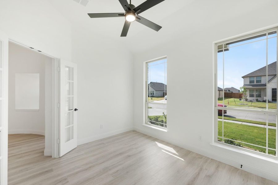Empty room with light wood floors, ceiling fan, tall windows, and a French door