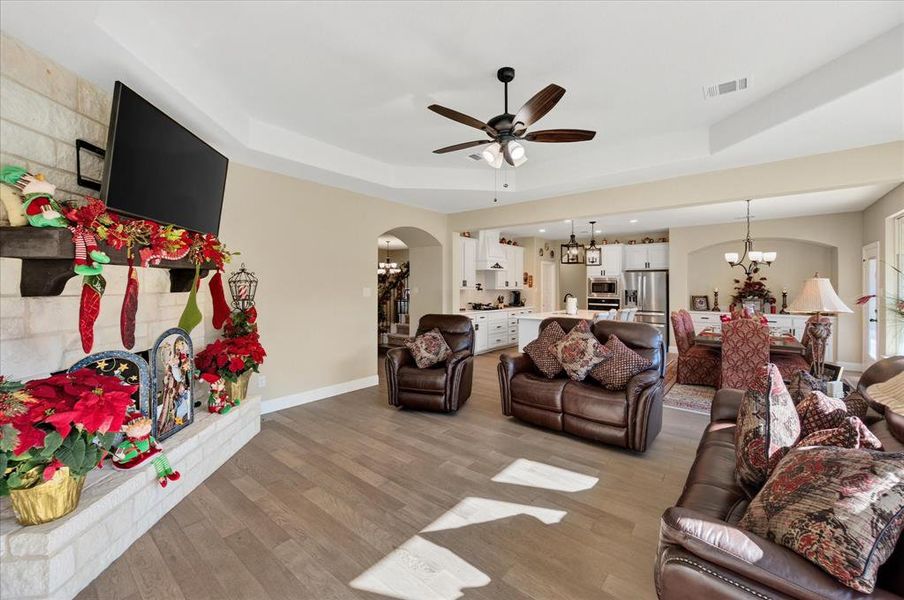 Living area featuring a chandelier, arched walkways, light wood finished floors, a tray ceiling, and ceiling fan Living area featuring a chandelier, arched walkways, light wood finished floors, a tray ceiling, and ceiling fan