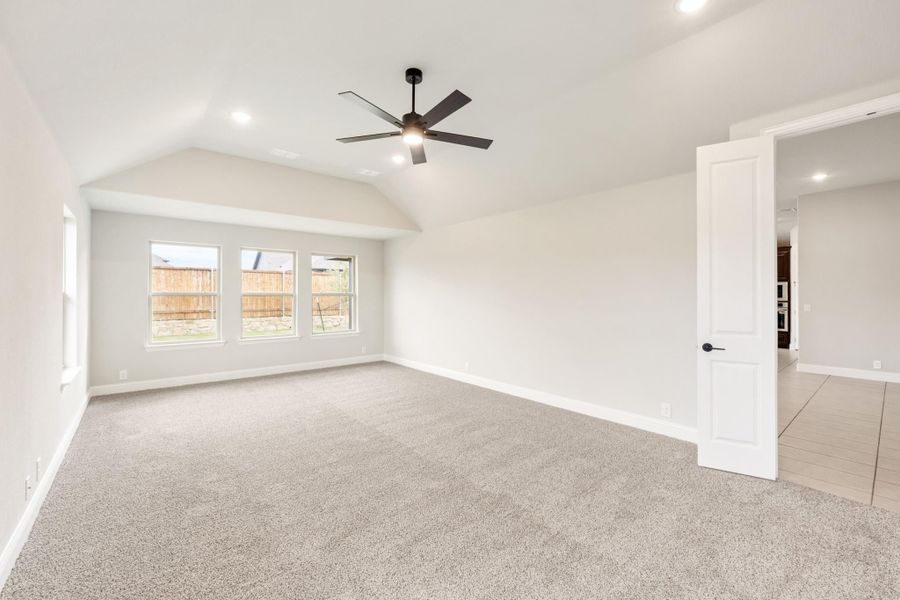 Empty bedroom with vaulted ceiling, ceiling fan, carpet flooring, and triple windows Empty bedroom with vaulted ceiling, ceiling fan, carpet flooring, and triple windows